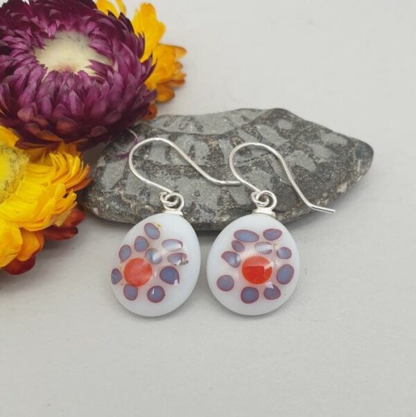 Fused glass earrings on silver war wires. The main colour is white with red random spots surrounded by grey