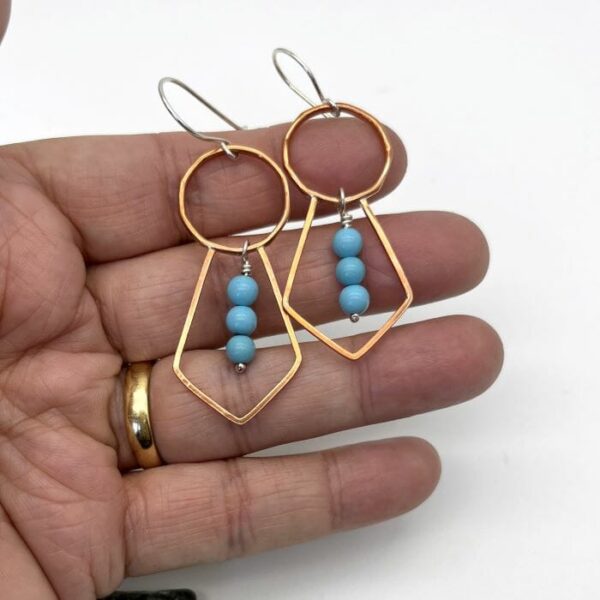 faceted hoop with rhombus/tie shaped drop all in copper with free moving turquoise beads hanging in the lower shape on silver ear wires