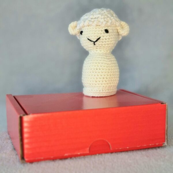 Crochet soft toy sheep on top of it's recyclable packaging