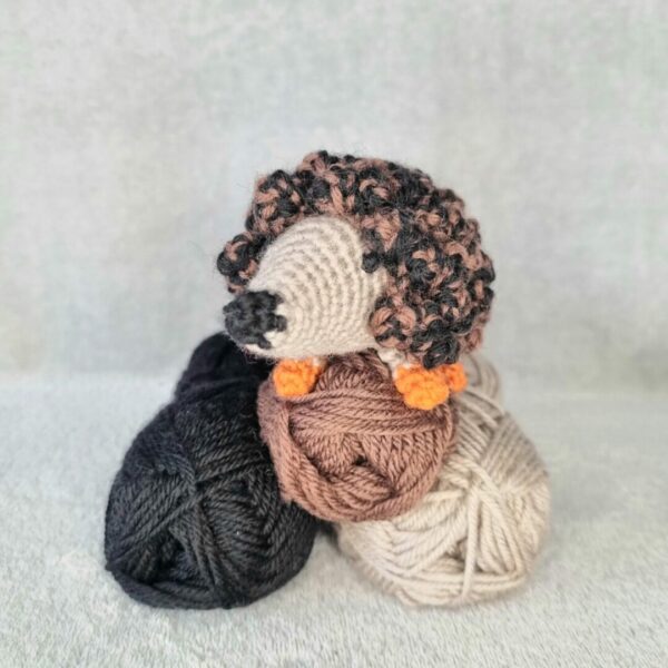 Handmade toy hedgehog sat on top of 3 balls of pure wool yarn