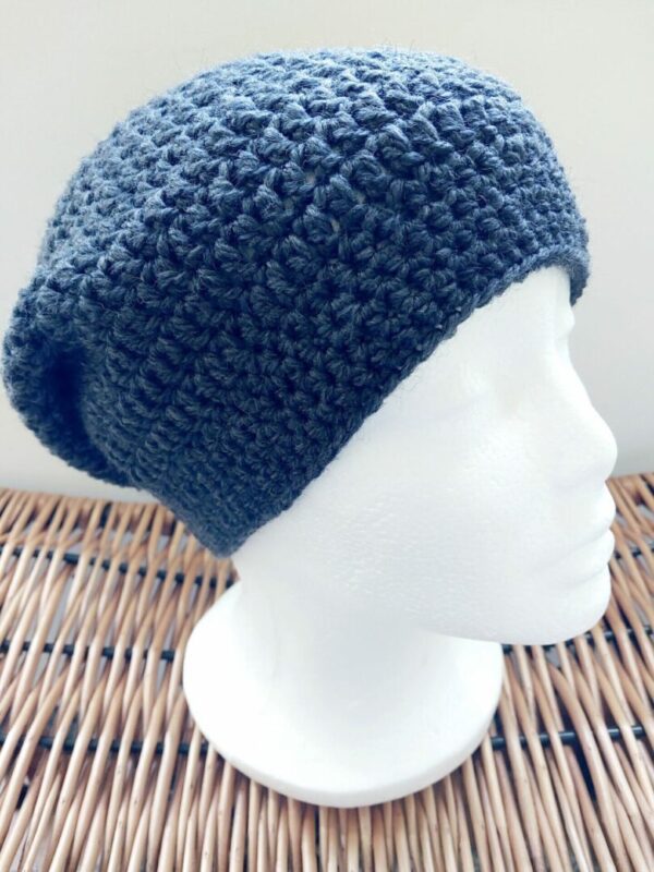 Dark petrol blue crochet slouchy beanie hat. Photographed on outside on a white mannequin head.