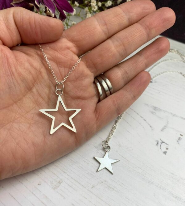 One open silver star shown on hand and and one solid star shown on white wooden background.