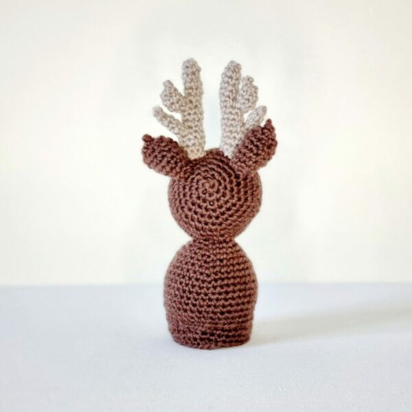 Rear view of a crochet brown reindeer soft toy on a white background