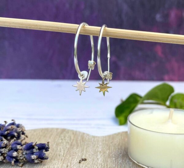 Silver hoops with star hanging from wooden stick with purple background, candle and lavender