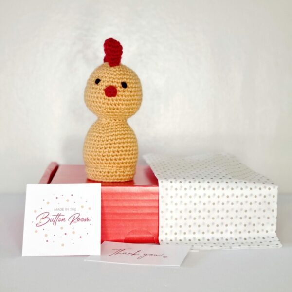 yellow and red crochet chicken sat on top of a red postage box with spotty tissue paper and business card