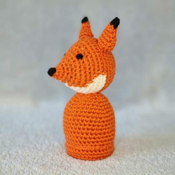 Side angle of a small orange fox soft toy. White chin and black tip ears on a light grey background.