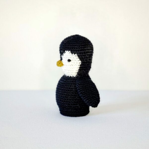 Side view of a small black and white crochet penguin on a white background
