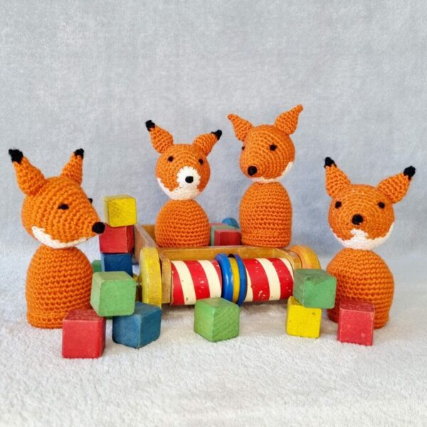 four orange foxes sat together around wooden children's blocks and small wooden truck with colourful wheels.
