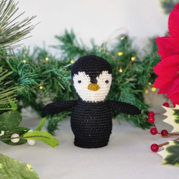 Small crochet black and white penguin with Christmas foliage around