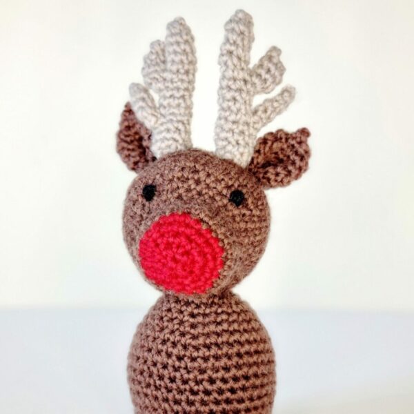 Close up head shot of Brown crochet reindeer with red nose on a white background