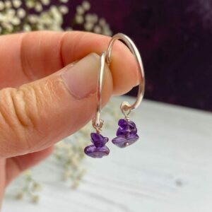 Amethyst crystal beads on silver hoops held in fingers with flowers in the background