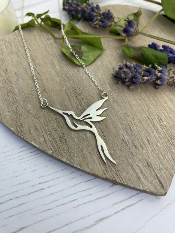 Silver hummingbird necklace on wooden background with lavender and leaves