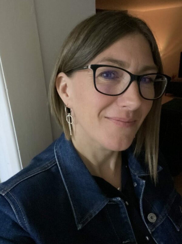 Girl with glasses wearing silver earrings and a denim jacket