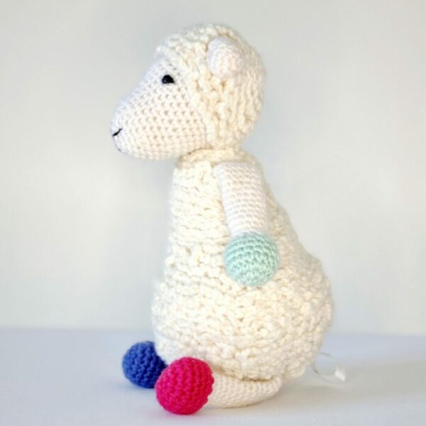 A large white crochet soft toy sheep sat down with red, blue and light green toes