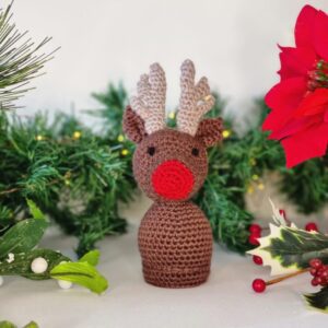 Brown reindeer with a red nose surrounded by Christmas foliage