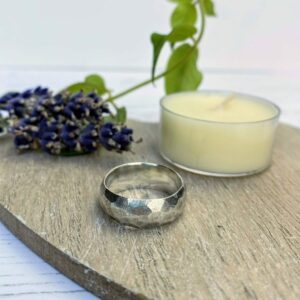 Silver thumb ring with facets all over on wooden surface with small candle and lavender next to it