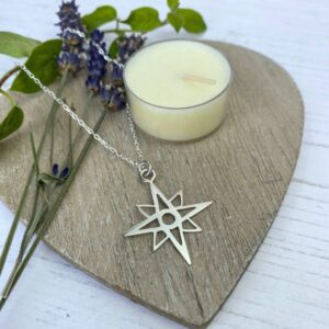 Silver star necklace on wooden heart with cream candle and flowers