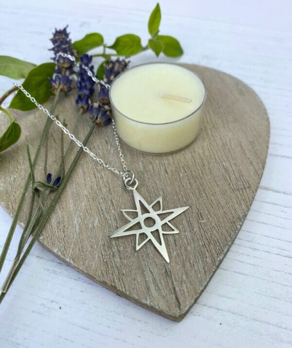 Silver star necklace on wooden heart with cream candle and flowers