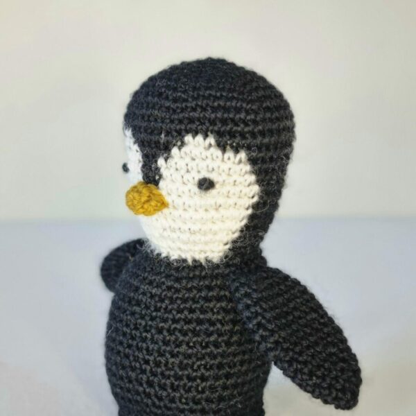 Close up side angle head shot of a black and white crochet penguin on a white background