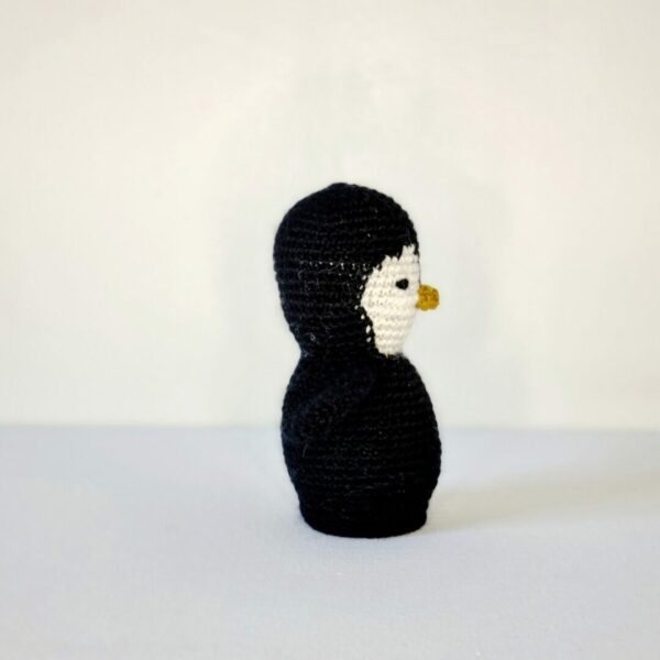 Side view of a small crochet black and white penguin on a white background