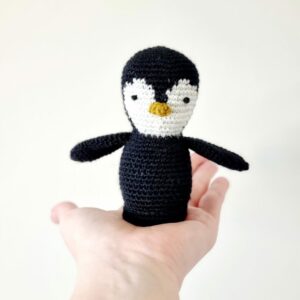 Small black and white crochet penguin sat in the palm of a hand with white background