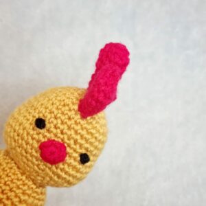 Head shot of a yellow crochet chicken popping it's head into view from the side.