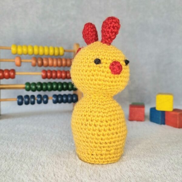 yellow and red crochet chicken sat next to vintage wooden abacas and blocks