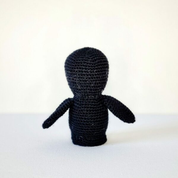 Back view of a black crochet penguin soft toy on a white background