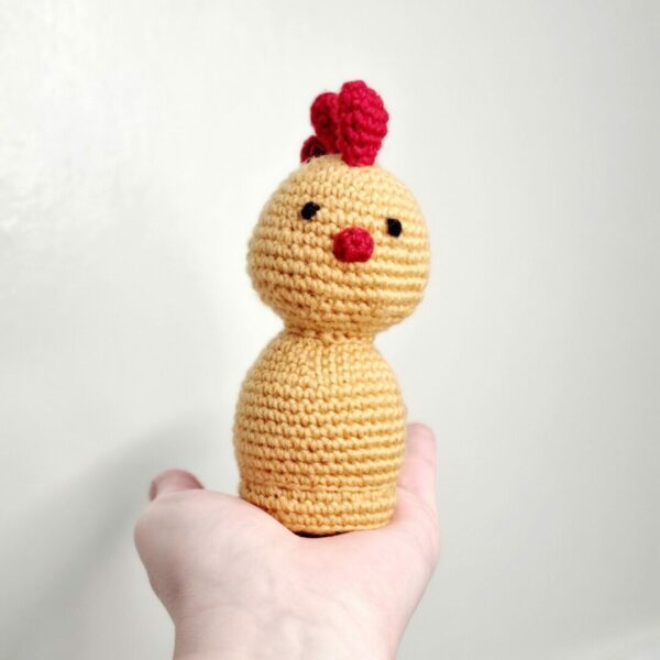 Crochet yellow and red chicken sat on a palm of a hand