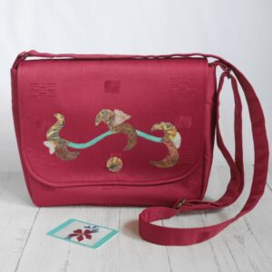 Deep red messenger style crossbody bag with abstract appliqued design on flap