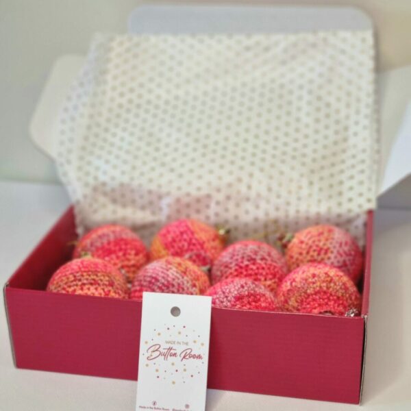 A red postage box full of pink and peach coloured baubles next to a business card
