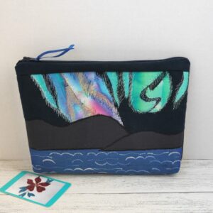 The front view of a zipped bag made from black fabric with a scene showing the Northern Lights over hills and sea made from appliqued and machine embroidered fabrics.