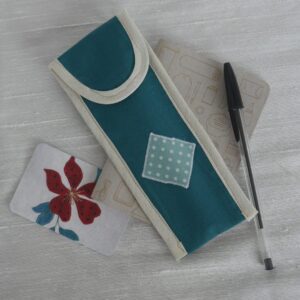 Green pen case with cream trim and appliqued design on front, shown with pen and small notebook