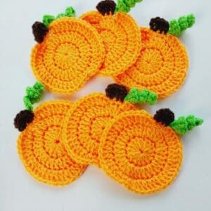 Set of six crochet pumpkin coasters. Orange circles with small brown stem and curled green vine to each.