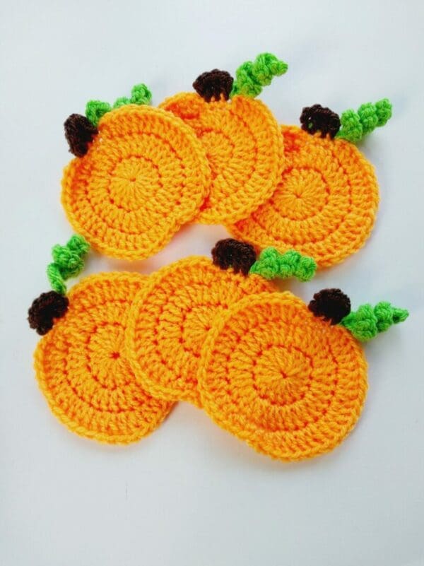 Set of six crochet pumpkin coasters. Orange circles with small brown stem and curled green vine to each.