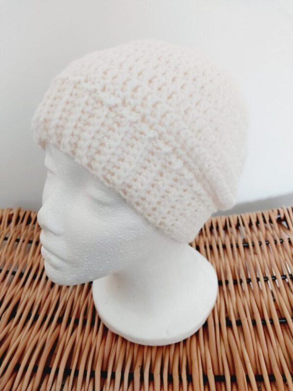 Light cream crochet beanie hat with brim, shown on a white mannequin head on brown wicker stool.