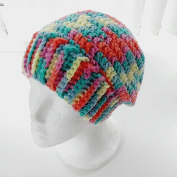 Multicoloured beanie hat with wide brim in rainbow yarn shown on white mannequin head.