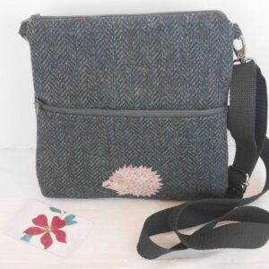 Dark wool tweed crossbody bag with zipped closure and hedgehog stitched onto front pocket.