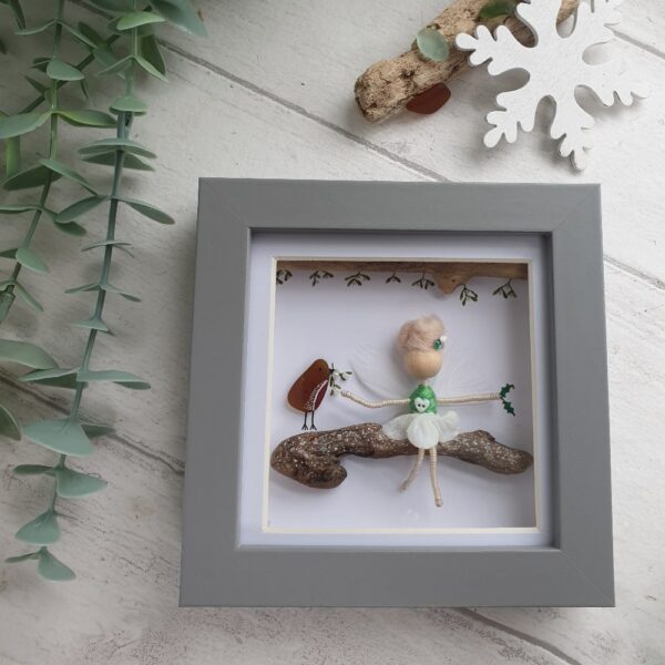 Mor Maids miniature fairy sitting on a driftwood branch with a robin red breast made using sea glass and branches of mistletoe above her. Framed in a grey box frame 12cm x 12cm.
