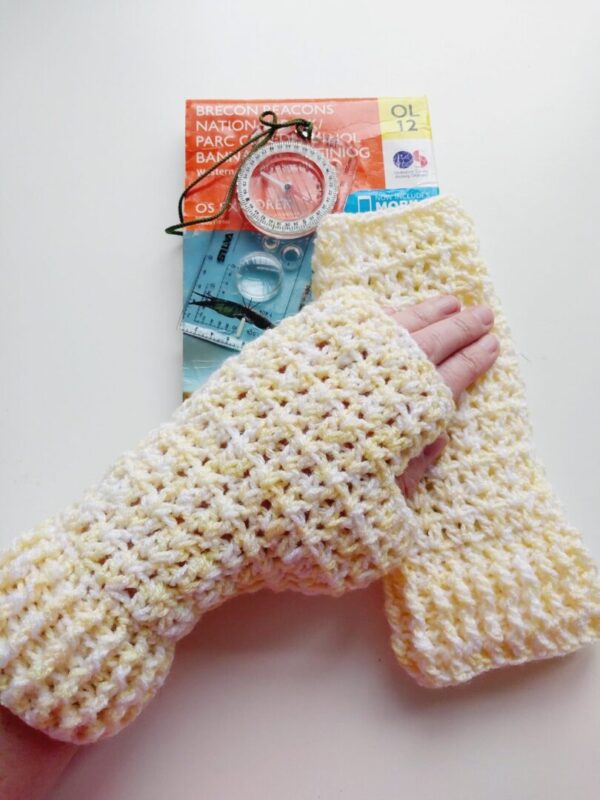 Yellow and White twisted yarn, crochet fingerless gloves, shown work on hand resting on top of an OS map.