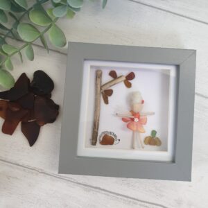 Cute fairy picture made using a Mor Maids miniature fairy with a pumpkin and hedgehog made of sea glass and a tree made using driftwood and seaglass. Framed in a grey box frame 12cm x 12cm.