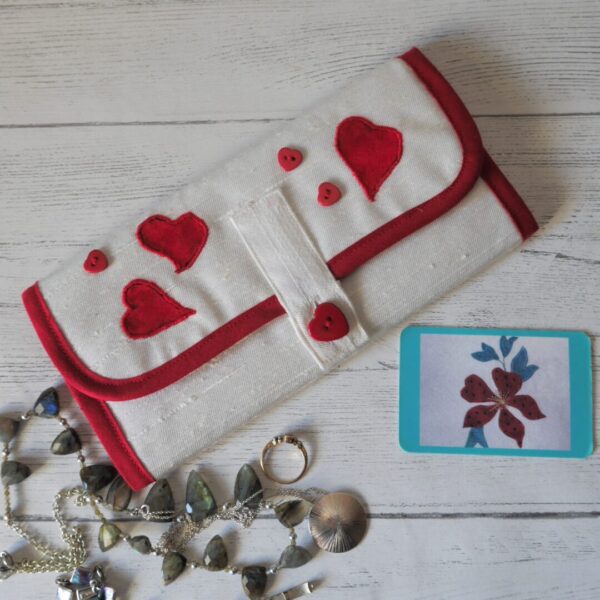 A white roll with red trim, appliqued red hearts and red heart-shaped button closure shown with a selection of jewellery