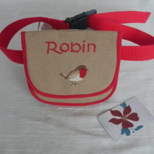 Small beige and red bum bag with a robin appliqued onto the flap and the word Robin machine stitched above it. Bag is shown on a red polypropylene belt.