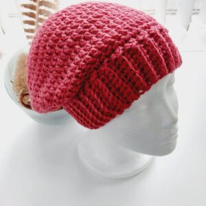 Crochet slouchy beanie hat in a rich red aran yarn called Berry. Photographed on a white mannequin head.