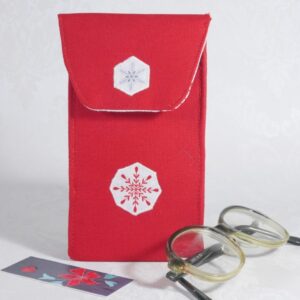 A small red glasses pouch with two snowflake designs appliqued onto the front, shown with a pair of child's spectacles.