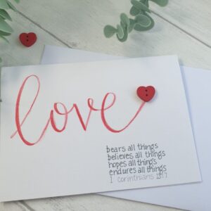 Hand lettered Calligraohy card - with Love in red letters and addition on red heart button and the bible verse from 1 Corinthians 13:7