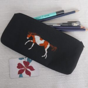Black pencil case with appliqued brown and white horse shown with pens and pencils emerging from zipped opening.