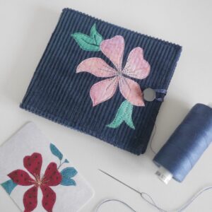 Needle case made from navy cord with pink clematis flower appliqued on front, shown with needle and thread