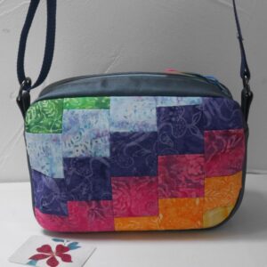 A zipped bag in a rounded rectangular box shape with a patchwork front made from rainbow coloured cotton fabrics.
