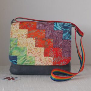Messenger style crossbody bag with flap made from patchwork of rainbow coloured fabrics arranged diagonally.